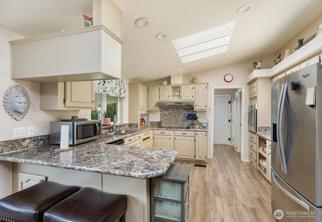 kitchen with lofted ceiling with skylight, under cabinet range hood, a sink, appliances with stainless steel finishes, and a peninsula