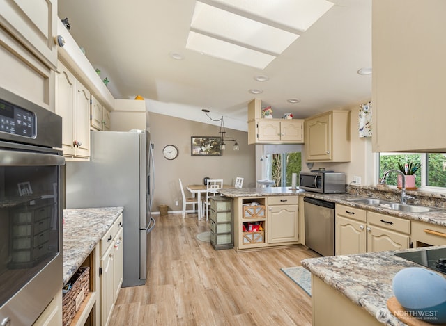 kitchen featuring appliances with stainless steel finishes, cream cabinets, a peninsula, light wood-style floors, and a sink