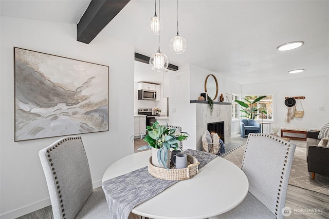 dining space with light wood-style flooring, a fireplace, beam ceiling, and baseboards