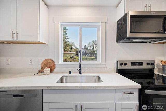 kitchen with appliances with stainless steel finishes, white cabinetry, a sink, and light stone countertops