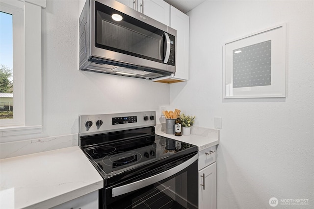 kitchen featuring stainless steel appliances, light stone counters, and white cabinetry