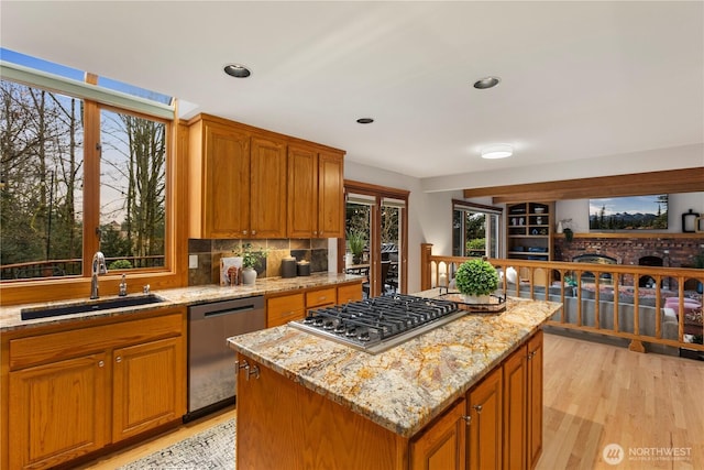 kitchen with light stone counters, a sink, appliances with stainless steel finishes, light wood-type flooring, and a center island