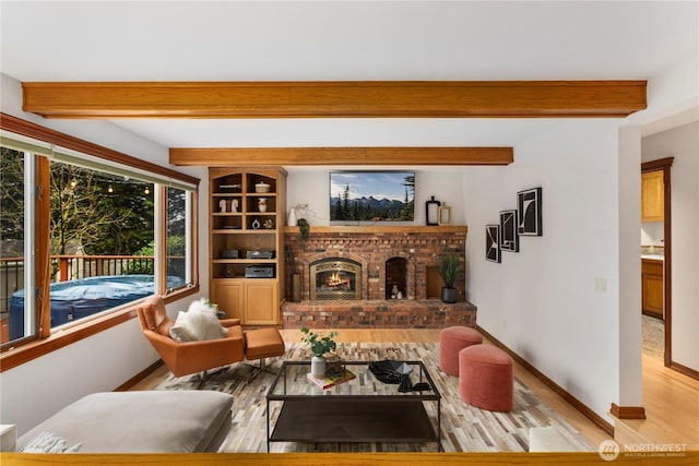 living room featuring a brick fireplace, beamed ceiling, baseboards, and wood finished floors