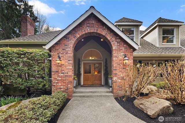 doorway to property with a shingled roof and brick siding