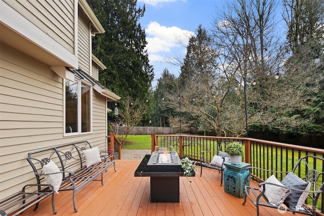 wooden deck with an outdoor fire pit, fence, and a lawn