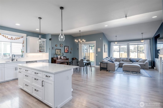 kitchen with white cabinets, a center island, light wood-style floors, pendant lighting, and a sink