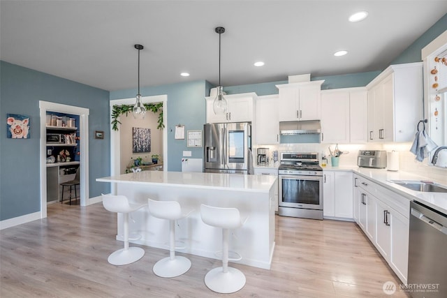 kitchen featuring a kitchen island, stainless steel appliances, under cabinet range hood, a kitchen bar, and a sink