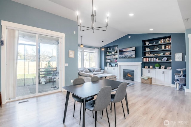 dining area featuring built in features, visible vents, light wood-style floors, a glass covered fireplace, and vaulted ceiling