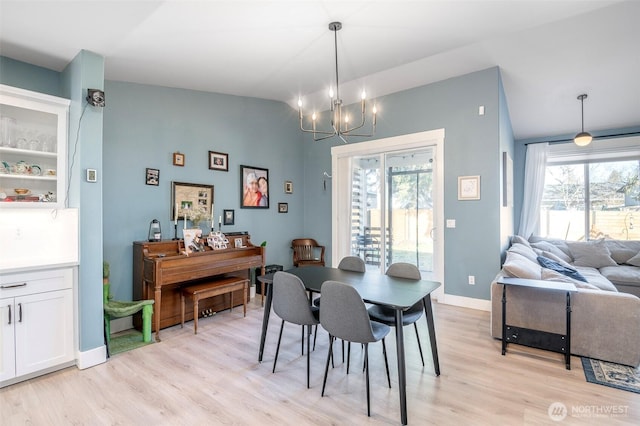 dining area featuring a chandelier, lofted ceiling, light wood-style floors, and baseboards