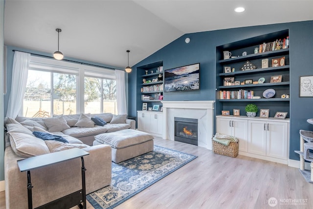 living area featuring vaulted ceiling, a glass covered fireplace, light wood-style flooring, and built in features