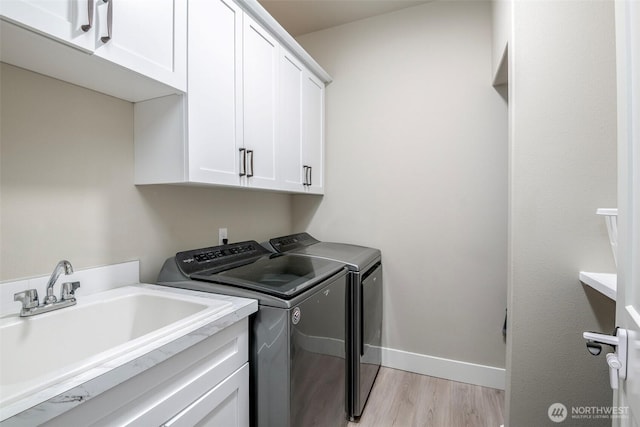 laundry room with cabinet space, light wood finished floors, baseboards, washer and dryer, and a sink