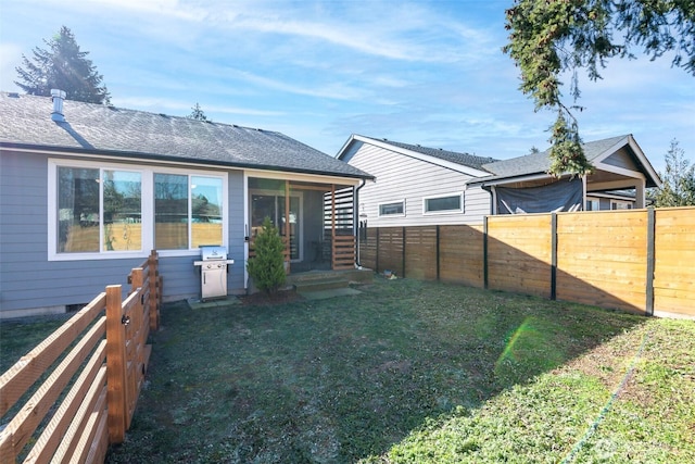 rear view of house with a fenced backyard, a lawn, and a shingled roof