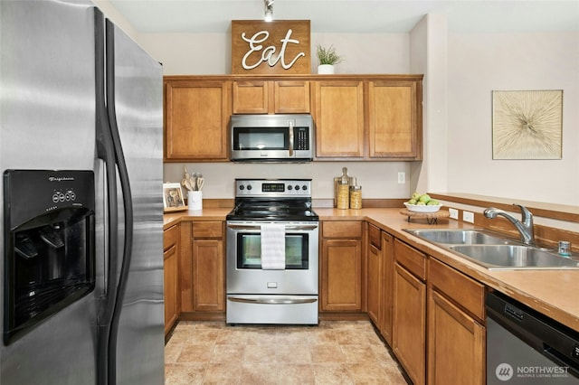 kitchen with light countertops, brown cabinets, a peninsula, stainless steel appliances, and a sink