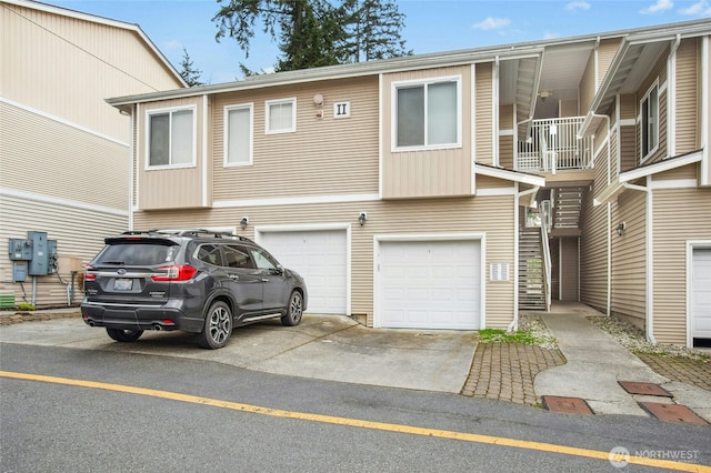 view of property with stairway, an attached garage, and driveway