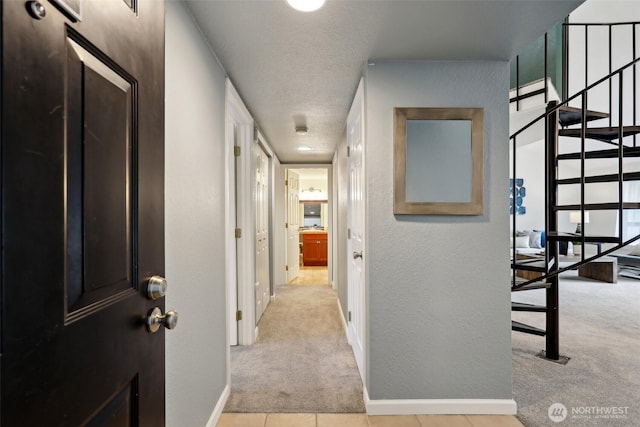 hall featuring a textured ceiling, a textured wall, light carpet, baseboards, and stairs