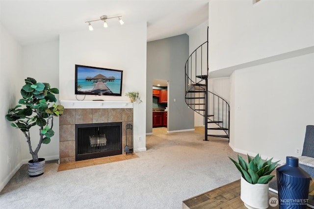 carpeted living area featuring high vaulted ceiling, a tile fireplace, baseboards, and stairs