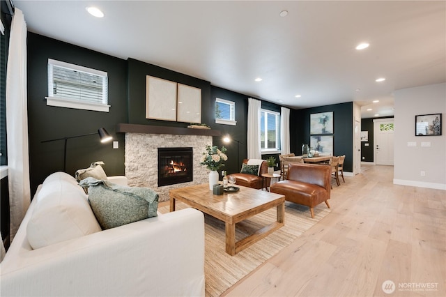 living area with light wood finished floors, a stone fireplace, baseboards, and recessed lighting