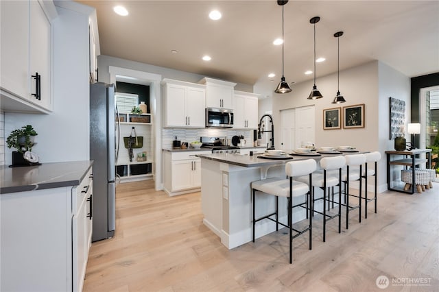 kitchen featuring appliances with stainless steel finishes, a kitchen bar, light wood-style flooring, and white cabinetry