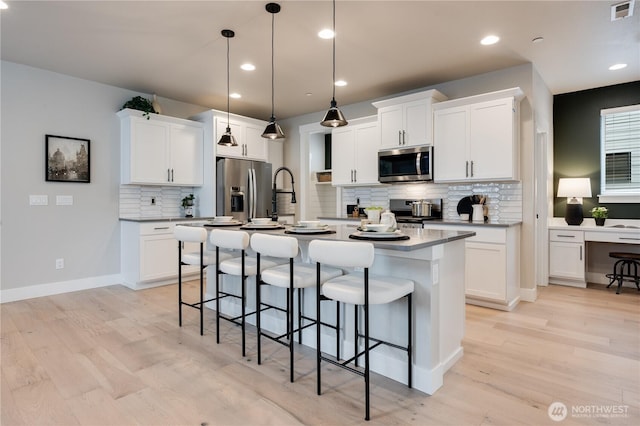 kitchen with visible vents, a kitchen breakfast bar, appliances with stainless steel finishes, light wood-type flooring, and a center island with sink