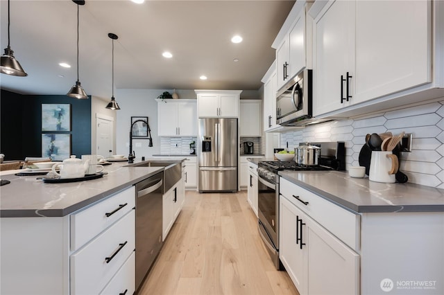 kitchen with a sink, white cabinetry, light wood-style floors, appliances with stainless steel finishes, and decorative light fixtures