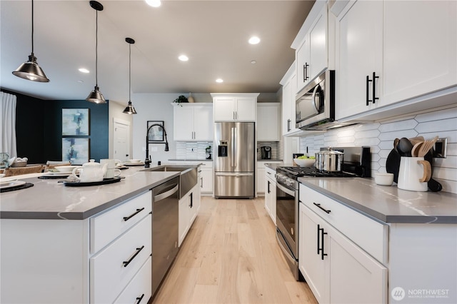 kitchen featuring pendant lighting, light wood finished floors, appliances with stainless steel finishes, white cabinetry, and a sink