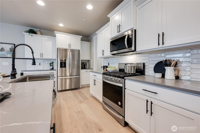 kitchen with backsplash, appliances with stainless steel finishes, white cabinetry, a sink, and light wood-type flooring