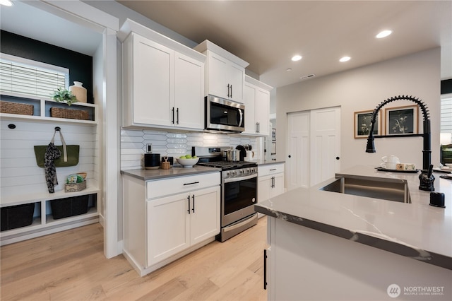 kitchen featuring appliances with stainless steel finishes, white cabinets, and light wood-style flooring