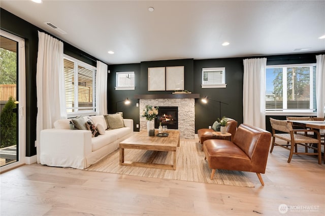 living room with light wood finished floors, a stone fireplace, and plenty of natural light