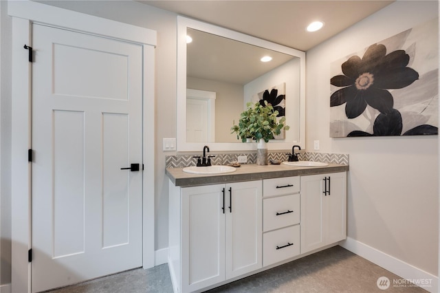 bathroom with double vanity, backsplash, a sink, and baseboards