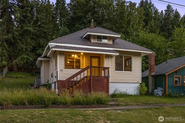 view of front facade featuring a porch, a front yard, metal roof, and a chimney