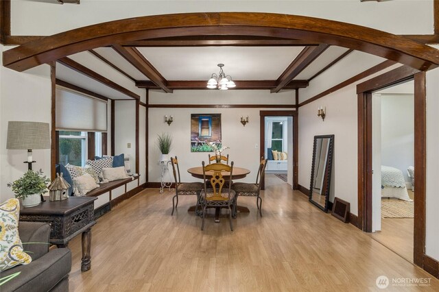 dining space with light wood-style floors, arched walkways, a chandelier, and beamed ceiling