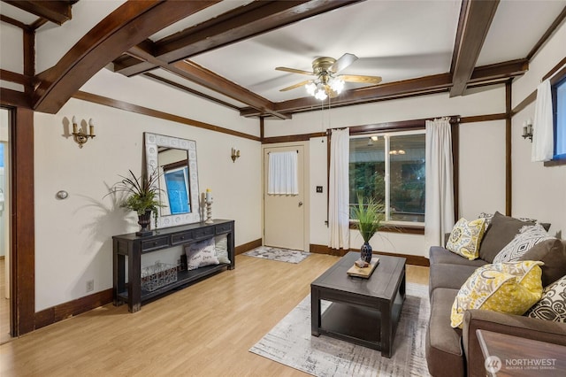 living area featuring a ceiling fan, beamed ceiling, light wood-style flooring, and baseboards