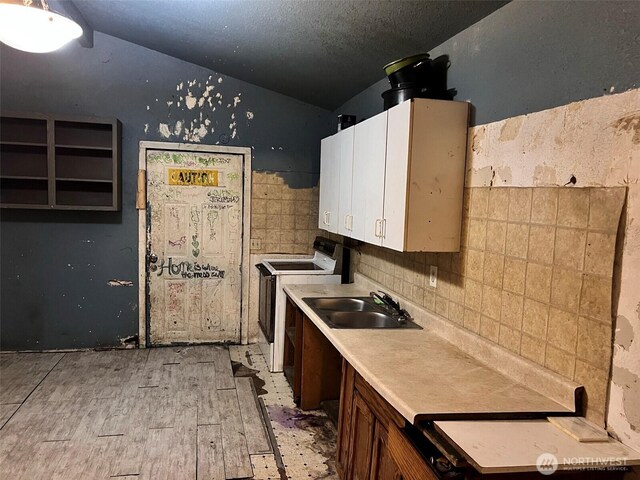 kitchen with lofted ceiling, electric range, a sink, backsplash, and light wood finished floors