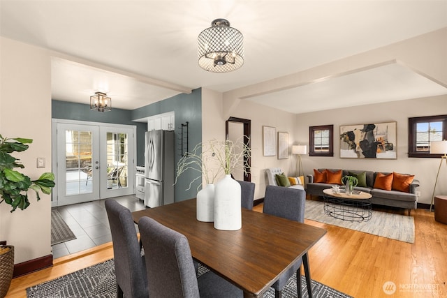 dining room with french doors, baseboards, light wood-type flooring, and an inviting chandelier