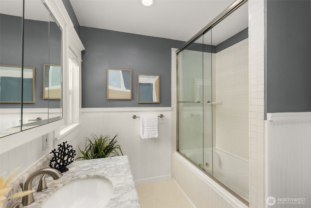 full bathroom with combined bath / shower with glass door, vanity, and wainscoting