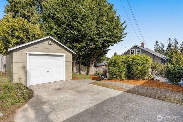 detached garage featuring concrete driveway and fence