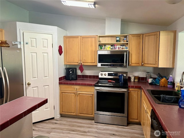 kitchen with vaulted ceiling, stainless steel appliances, a sink, and light wood-style flooring