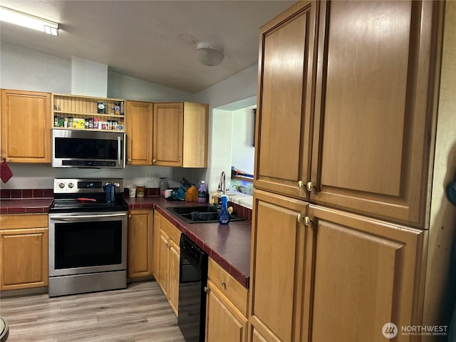 kitchen with dark countertops, light wood-style flooring, vaulted ceiling, stainless steel appliances, and a sink