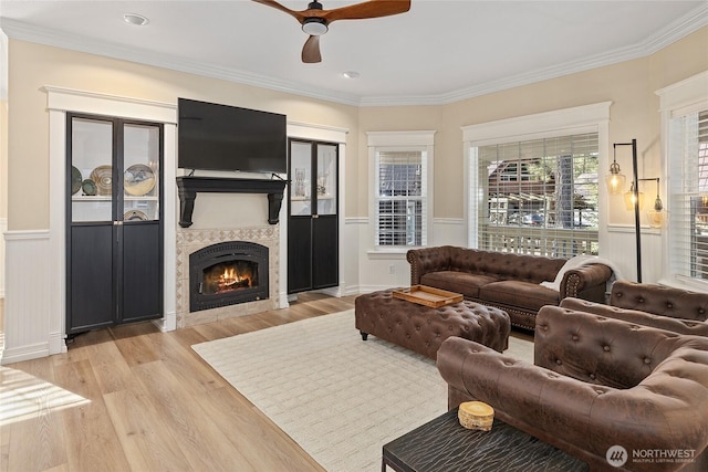 living area featuring crown molding, wainscoting, light wood finished floors, and ceiling fan