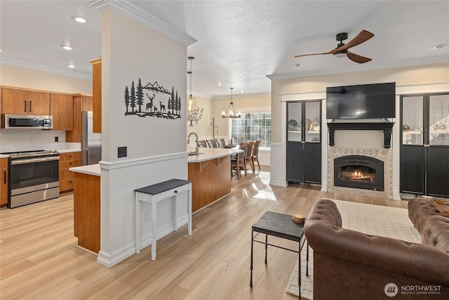 living area featuring ornamental molding, light wood-style floors, a textured ceiling, a glass covered fireplace, and ceiling fan with notable chandelier