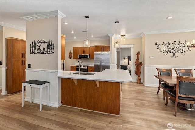 kitchen with light wood-style flooring, stainless steel appliances, a peninsula, a breakfast bar area, and brown cabinetry