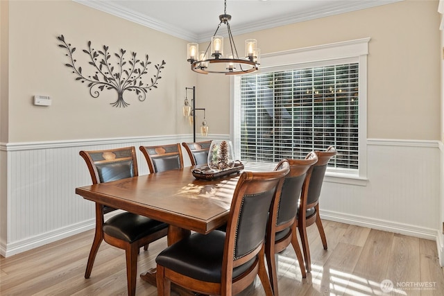 dining space featuring an inviting chandelier, crown molding, light wood finished floors, and wainscoting