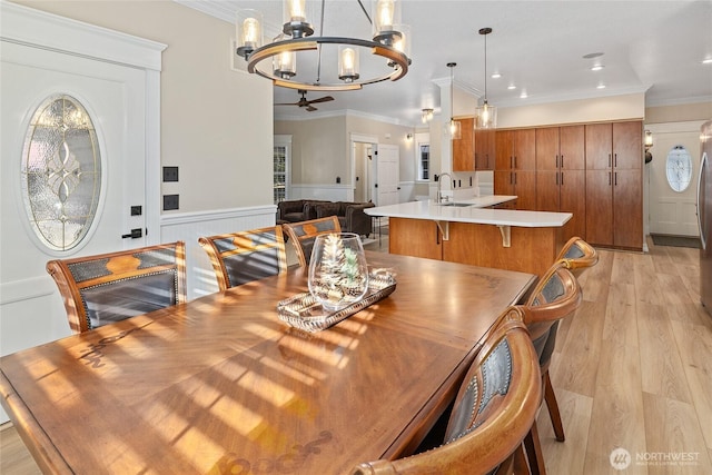 dining space featuring light wood-type flooring, a wainscoted wall, ornamental molding, ceiling fan with notable chandelier, and recessed lighting