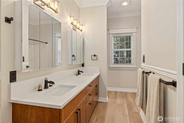 bathroom featuring a sink, baseboards, wood finished floors, and ornamental molding