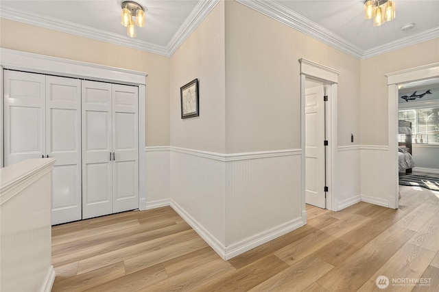 foyer with light wood-style floors, a wainscoted wall, and ornamental molding