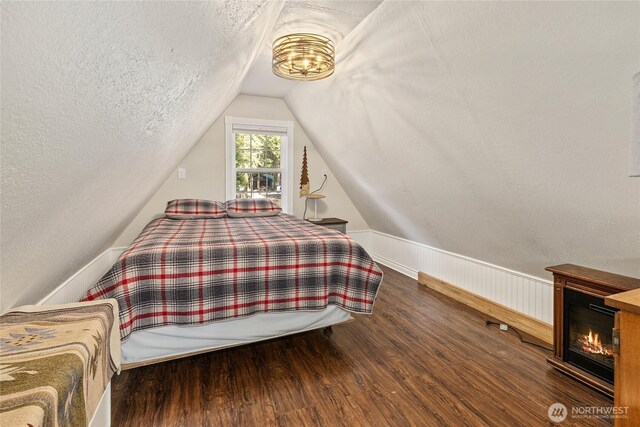 bedroom featuring a glass covered fireplace, vaulted ceiling, wood finished floors, and a textured ceiling