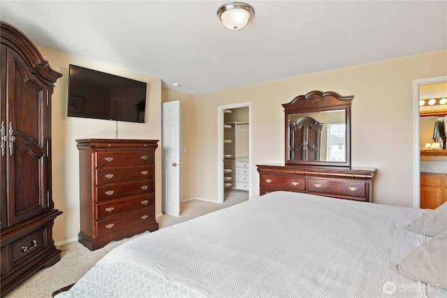 bedroom featuring a walk in closet, light carpet, baseboards, and ensuite bathroom