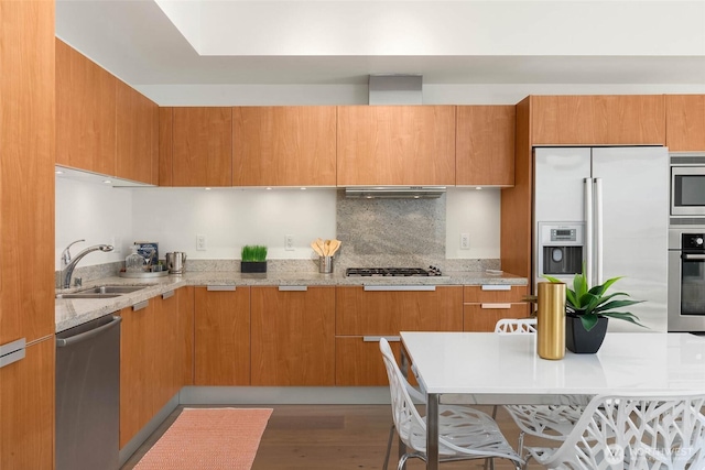 kitchen featuring stainless steel appliances, a sink, ventilation hood, brown cabinets, and modern cabinets