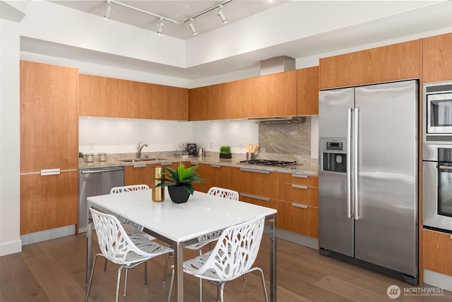 kitchen featuring appliances with stainless steel finishes, decorative backsplash, wood finished floors, and brown cabinets