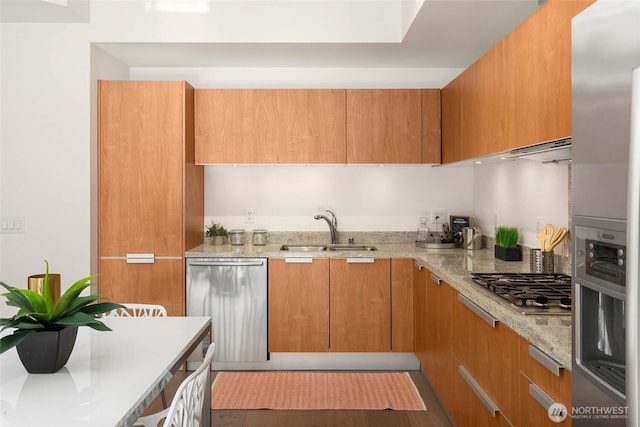 kitchen with light stone counters, a sink, appliances with stainless steel finishes, brown cabinets, and modern cabinets